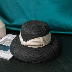 Close-up of black wide brim straw sun hat with cream ribbon bow and golden metal tag