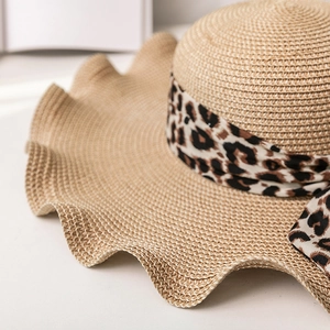 Close-up of beige straw sun hat with wavy brim and stylish leopard print ribbon