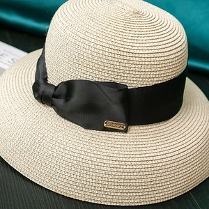 Detailed macro view of beige straw sun hat with black grosgrain ribbon and gold metal plate