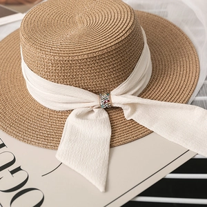 Detail of flat top straw hat featuring elegant cream ribbon and colorful rhinestone buckle