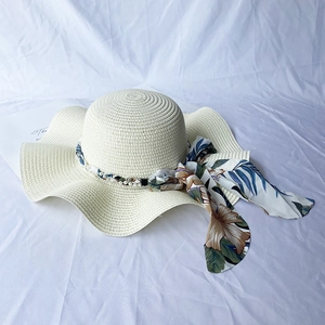 Detail of wide brim straw sun hat with pearl trim and floral ribbon on a white fabric