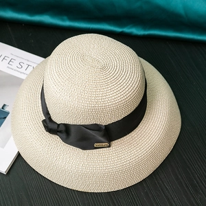 Detailed view of woven straw sun hat texture with elegant black ribbon bow and metal accent