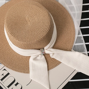 Detailed close-up of straw hat featuring white chiffon ribbon and crystal buckle