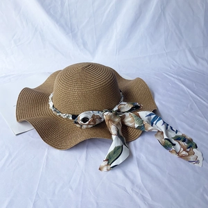 Detail of a brown straw sun hat featuring a wavy brim, floral ribbon, and pearl accent