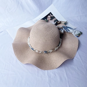 Detail of straw sun hat with pearl strand and floral ribbon on white fabric background