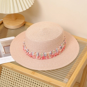 Detail of beige flat top straw hat with colorful bohemian tassel trim on a glass table