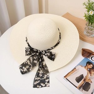 Detail of wide brim straw hat featuring pearl chain and floral ribbon on a table