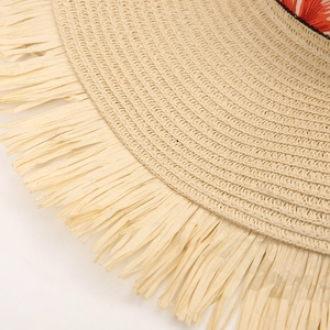 Close-up of woven straw hat featuring fringe edges and orange floral ribbon detail