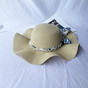 Close-up of khaki straw sun hat featuring wavy brim and elegant pearl scarf detailing