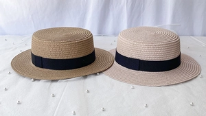 Detailed straw weave textures of khaki and beige flat top boater hats with black ribbons