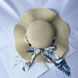 Detail of a straw sun hat featuring wavy brim, floral ribbon, and pearl accents on white cloth