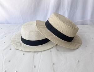 Flat top straw boater hats with black ribbon bands on white fabric with pearl accents