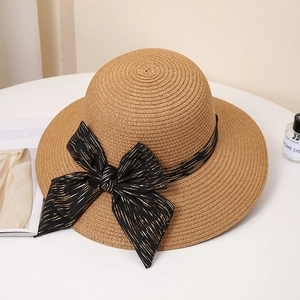 Brown woven straw sun hat with large black gold-striped bow on a white table