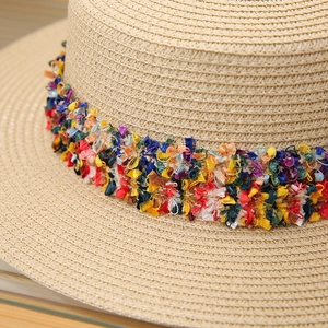 Close-up of bohemian colorful tassel ribbon on flat top straw beach sun hat texture