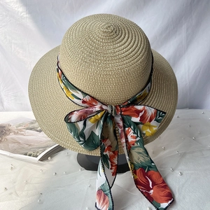 Détail d'un chapeau de paille d'été avec un grand ruban floral sur un tissu blanc