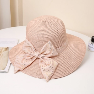 Detail of pink straw hat with gold-striped bow on elegant white table setting