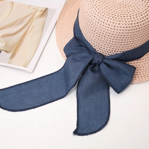 Detail of light beige straw hat featuring a wide navy grosgrain bow with long ribbons