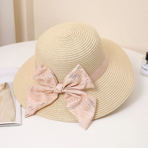 Detail of light beige woven straw hat featuring a large pink bow and fine metallic accents