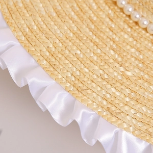 Detail of straw sun hat featuring elegant white ruffle ribbon and pearl decorations