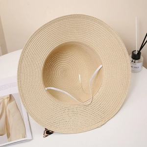 Detail of straw sun hat with leopard print ribbon and white windproof strap on a table