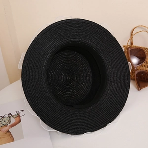 Detail of black straw hat featuring white wavy mesh trim and woven texture in a summer setting