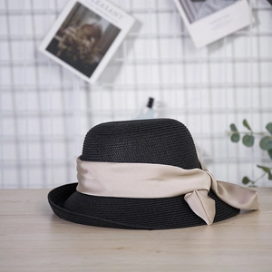 Detail of a black woven straw sun hat featuring a wide champagne satin ribbon bow