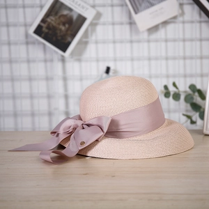 Detail of pink straw sun hat featuring a large elegant silk bow on a wooden surface