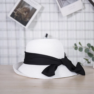 Detail of white woven sun hat with wide black chiffon bow on light wooden surface