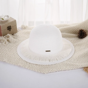 Detail of white woven straw hat with frayed edges and peace metal tag on knit blanket