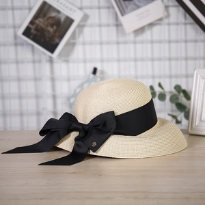 Detailed view of women's straw sun hat with black ribbon bow and gold logo detail