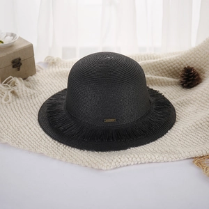 Close-up of black straw sun hat with fringe edge and small gold logo on knit blanket