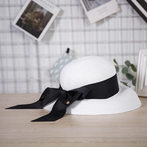 Elegant white straw hat with black grosgrain ribbon and golden buckle on wooden surface