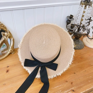 Flat top raffia straw hat with frayed edges and a black ribbon bow for summer beach sun protection
