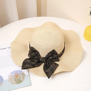 Vue détaillée du chapeau de paille à bord ondulé avec ruban noir et nœud rayé doré