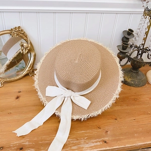 Detail of raffia sun hat with white ribbon bow and raw fringe edge on wooden table