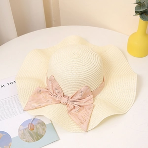 Détail d'un chapeau de paille à bord ondulé et nœud rose avec des accents rayés dorés