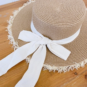 Close-up of a raffia boater hat with frayed edges and an elegant cream ribbon bow
