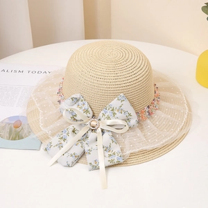 Détail d'un chapeau de paille avec nœud floral, boucle en perle et bordure en dentelle