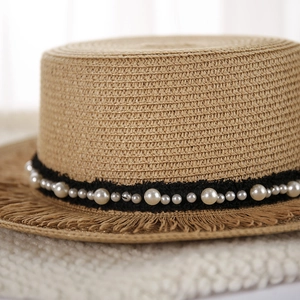 Dettaglio di cappello in paglia intrecciata a mano con perle e bordo a frange