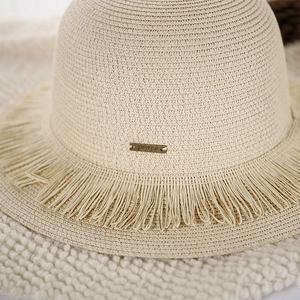 Detailed texture of woven straw hat with fringe edge and peace engraved metal plaque