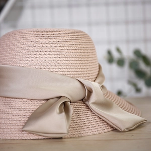 Detailed view of pink straw sun hat showing fine weave texture and champagne satin bow