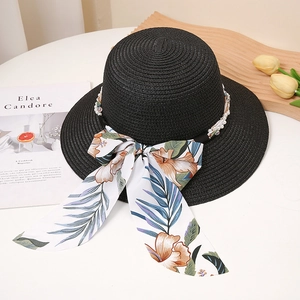 Détail d'un chapeau de paille noir avec perles blanches et ruban floral sur fond blanc