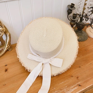 Women's raffia boater hat with frayed edges and wide ribbon bow for summer beach sun protection