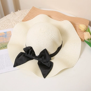 Beige wide-brim straw hat with black silk bow on wave-shaped wooden tray with tulips