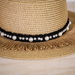 Dettaglio cappello di paglia intrecciata con nastro di perle e bordi sfrangiati