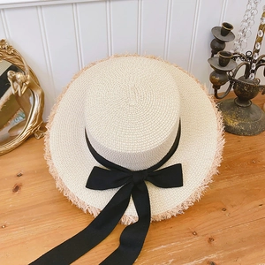 Close-up of beige raffia boater hat with black ribbon and frayed edges on wooden surface
