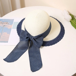 Close-up of beige straw sun hat featuring navy blue ribbon bow and lace contrast edging