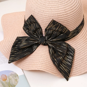 Détail d'un chapeau de paille rose avec un grand nœud noir aux reflets dorés