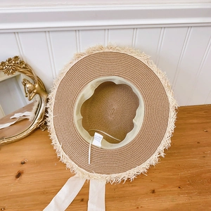 Detail of raffia straw hat with frayed edges, green sweatband and white ribbon strap