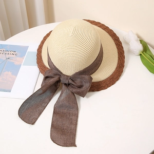 Flat lay of a two-tone straw hat with a large brown ribbon bow on a white desk